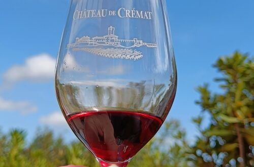 A glass of wine held up to the sky, holding a small measure of red wine. The glass reads "Chateau de Cremat", one of the vineyards near nice