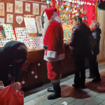 a man in a red Santa suit standing in front of a Christmas Market chalet in Strasbourg, France in Strasbourg's Christmas Markets