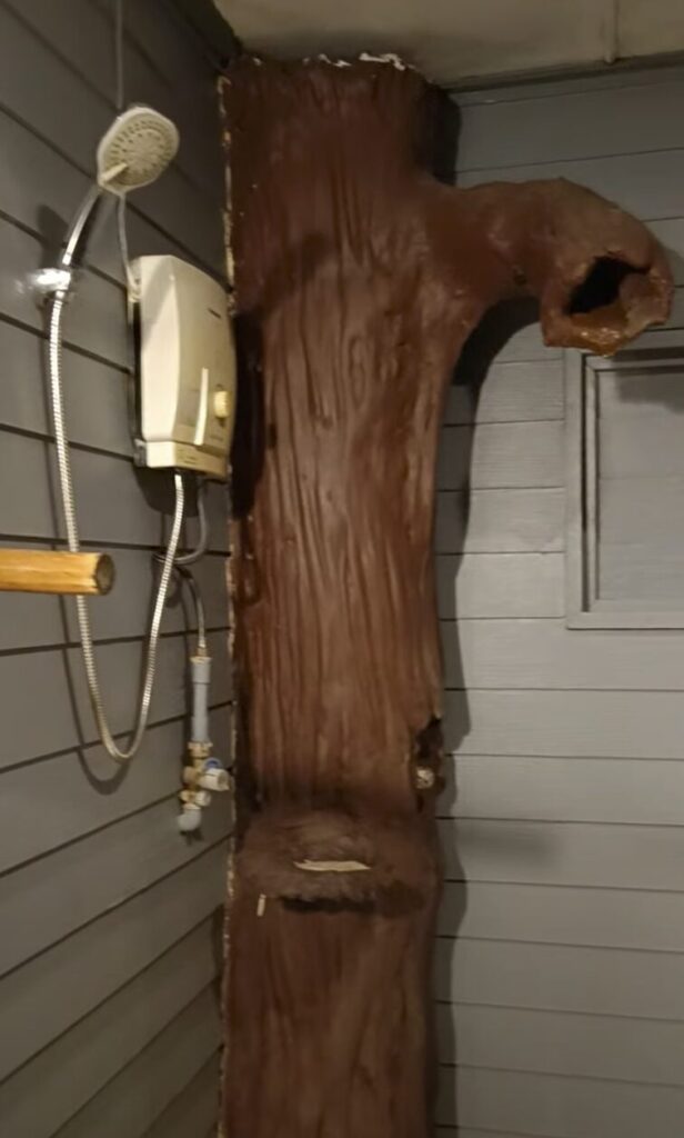 a brown fake tree trunk in a bathroom that serves as the shower