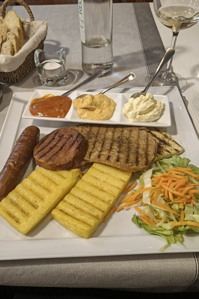 The vegan mixed grill dish in La Lanterna, vegan restaurant in verona. The dish shows grilled polenta, a seitan steak, veggie sausage and homemade condiments. 