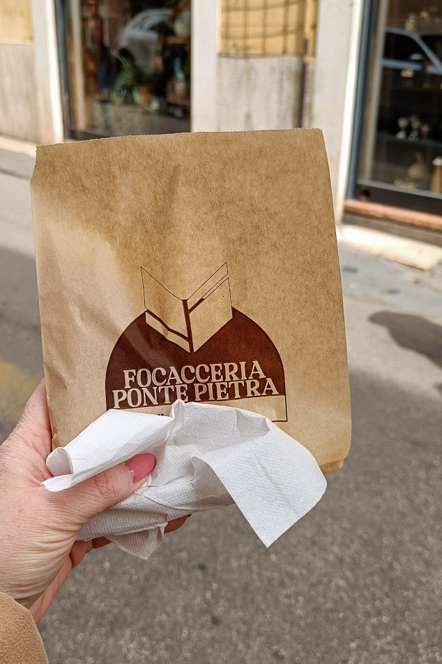 A hand holding a brown paper bag that has the words "focacceria ponte pietra" printed on it