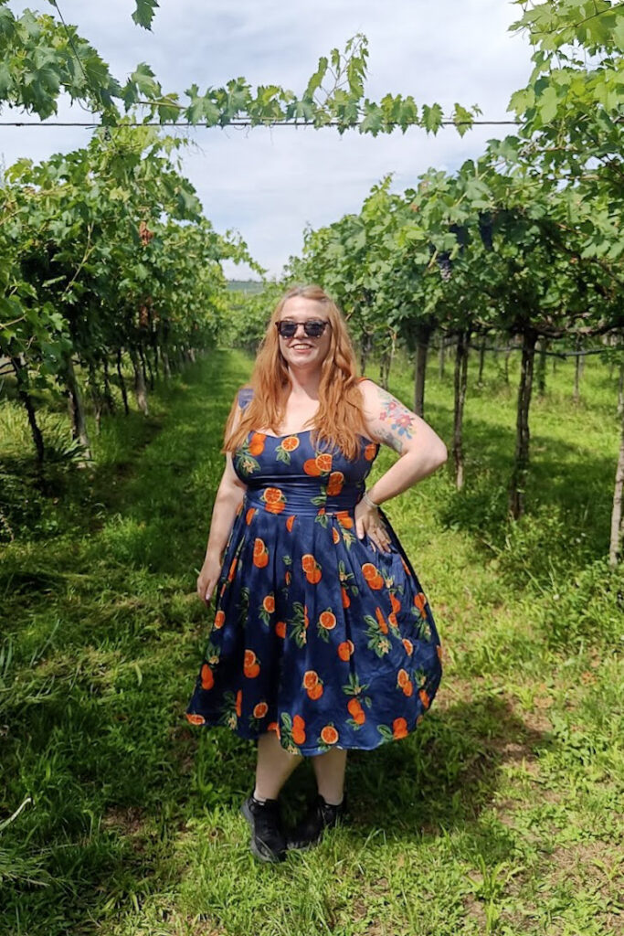 Laura in a navy dress with orange print, standing in a Valpolicella winery vineyard