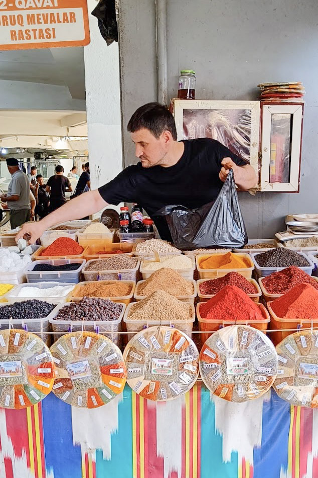 A man at a market stall in Uzbekistan, filling a bag with spices