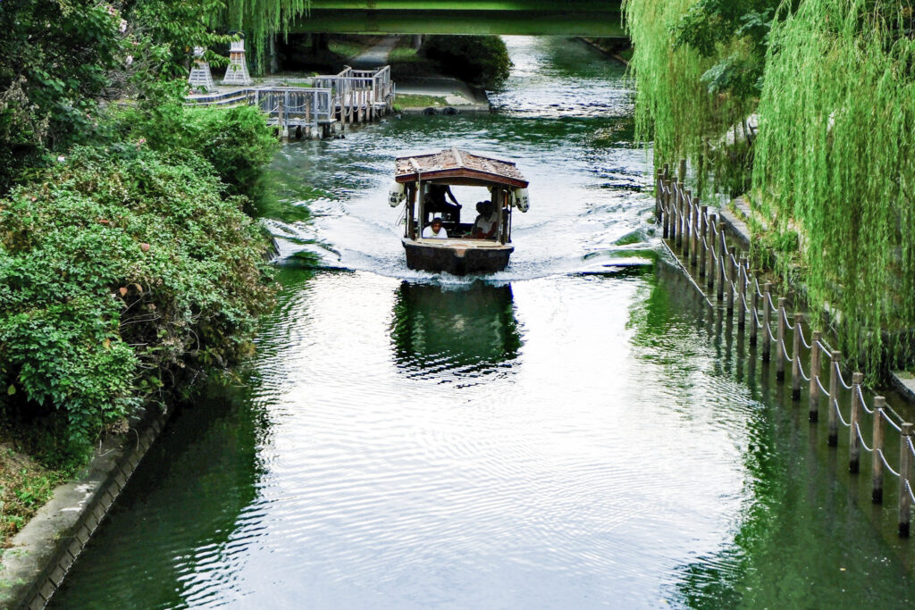 A flat bottomed canal boat sailing by weeping willows in Fushimi, Japan
