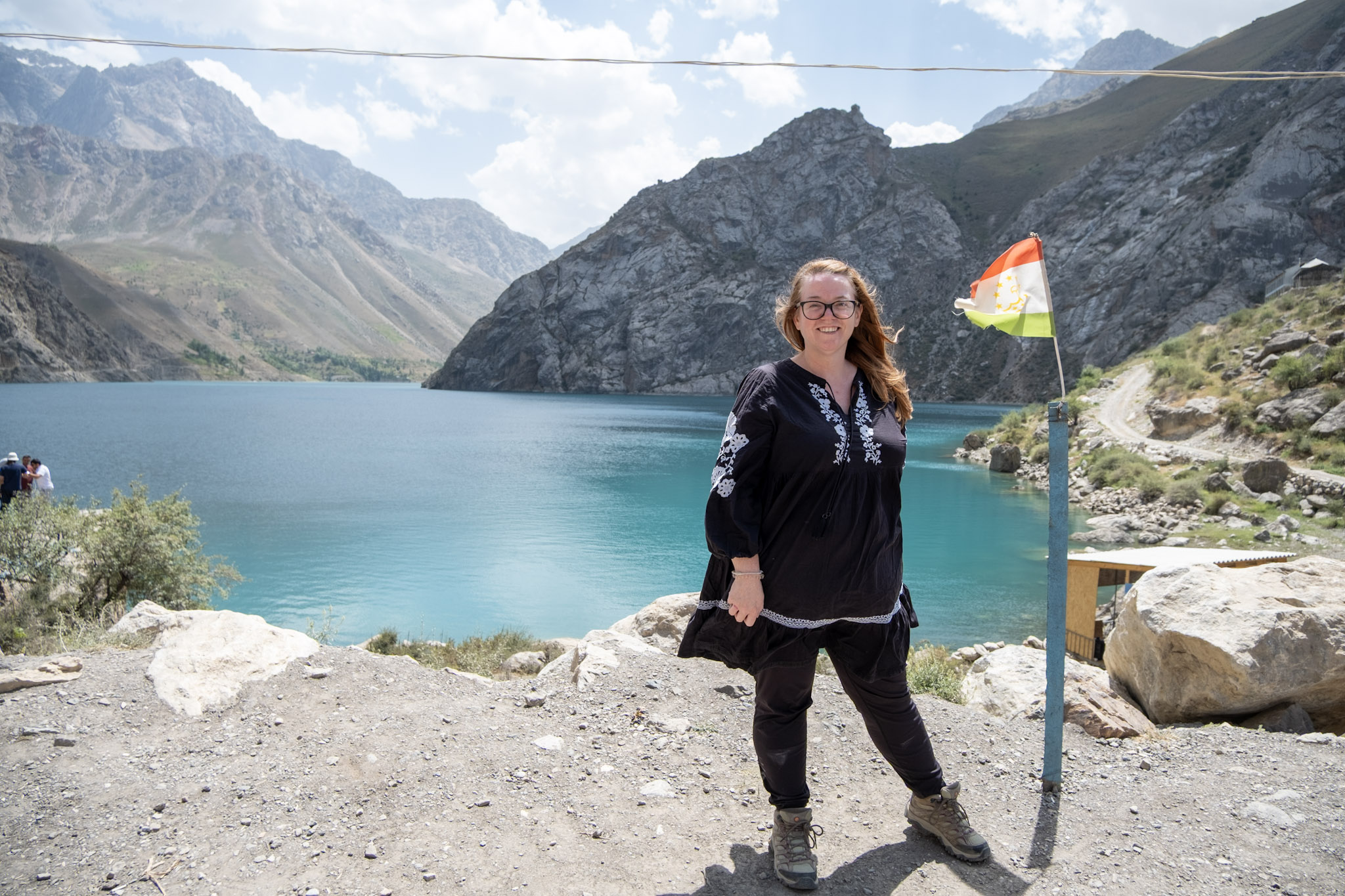 Red haired woman standing next to a flagpole by a lake